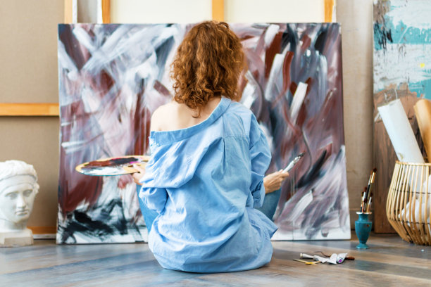 女艺术家坐在工作室的地板上画画图片下载