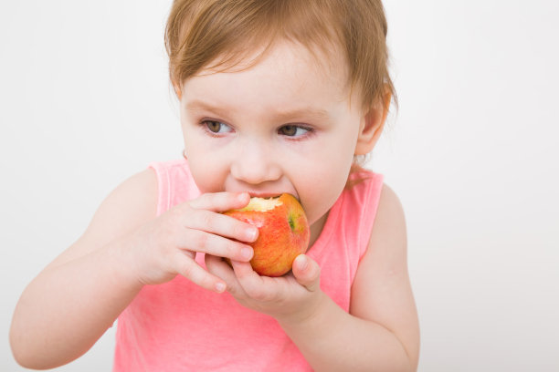 女婴吃苹果孤立在浅灰色背景。新鲜水果。特写镜头。前视图。图片下载