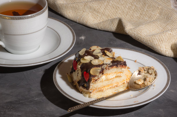 静物层次的自制海绵蛋糕和一杯红茶在一个白色的盘子，和亚麻餐巾，黑色的背景，强光，照片在一个低的关键。图片下载