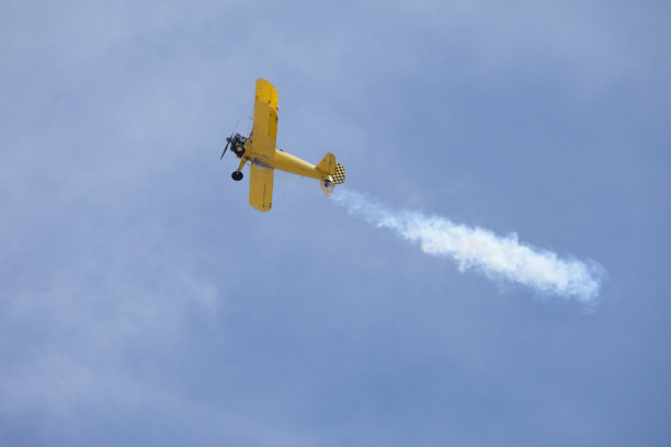 亮黄色双翼飞机向上飞行，身后有烟迹图片下载