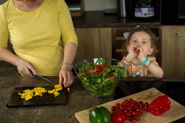 小女孩在吃樱桃番茄，妈妈在准备蔬菜沙拉，幽默的照片图片下载