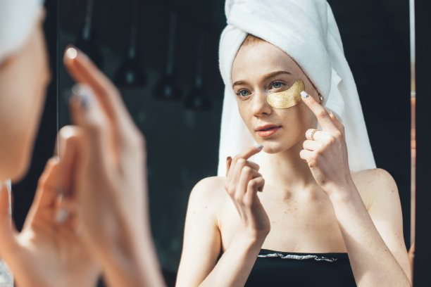 一名长雀斑的白人女性在洗澡后在眼睛下面敷上金色水凝胶眼罩，并用毛巾盖住头部图片下载