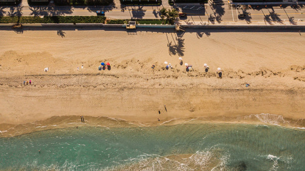 2021年3月春假期间，佛罗里达州棕榈滩海滩上的漂亮的粉红色沙滩伞、人们、棕榈树的阴影图片下载