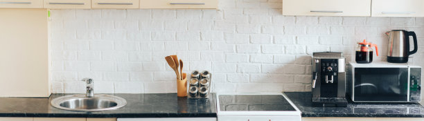 轻厨房设计，白色砖围裙。黑色大理石柜台上放着厨房用具。长长的横幅图片下载
