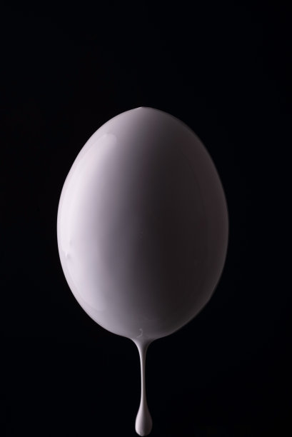 白色的鸡蛋在黑色的背景上滴着白色的颜料。简约的复活节的概念图片下载