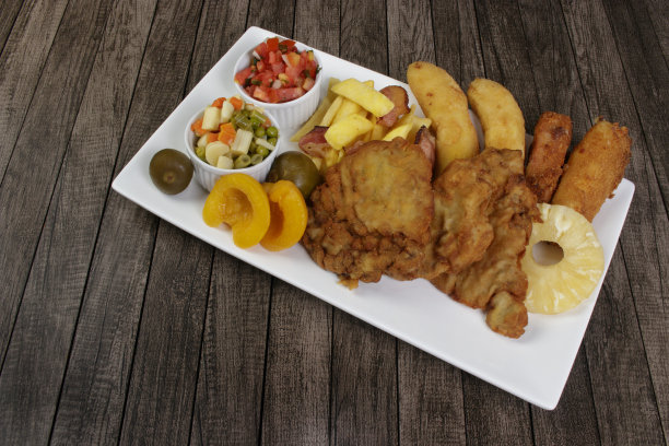古巴鱼片。由面包屑牛排，香蕉，面包屑奶酪和火腿制成。薯条配培根。油醋酱、蔬菜和水果。放在瓷盘上。特写照片与文字空间。图片下载