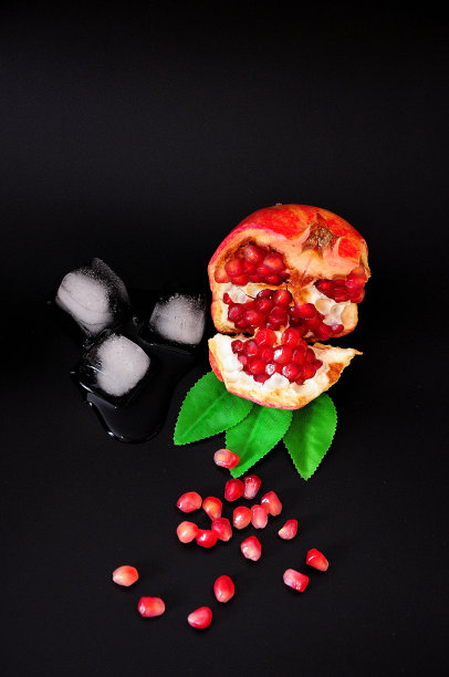 带叶子和冰块的熟透的石榴，在黑色的背景上，在砂子里。图片下载