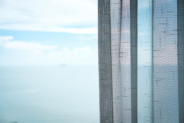 拉近，窗帘在酒店房间里，模糊了海和天空的背景。图片下载