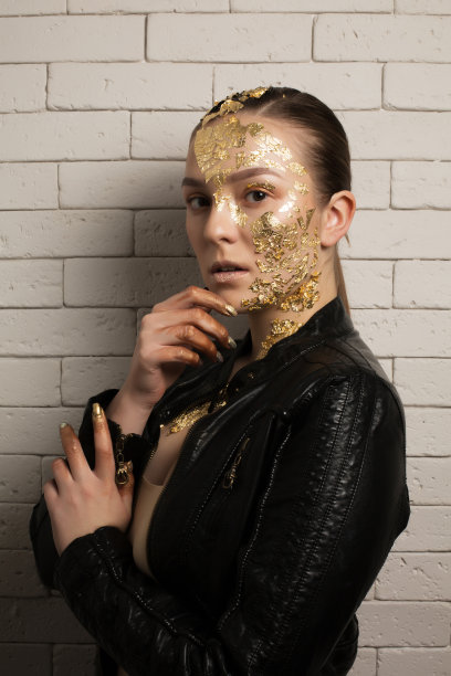 时尚镜头优雅的黑发女子与金箔在她的脸和颈部，穿着皮夹克图片下载