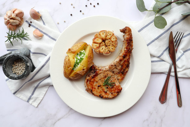 烤猪排配烤土豆和烤大蒜，配上一些配料，放在白色盘子里，大理石背景。俯视图图片下载