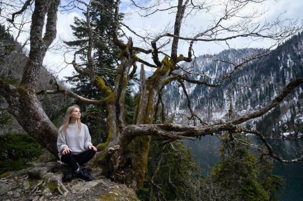 女孩坐在一棵树上，在蓝色的湖背景上沉思。阿布哈兹的Ritsa湖图片下载