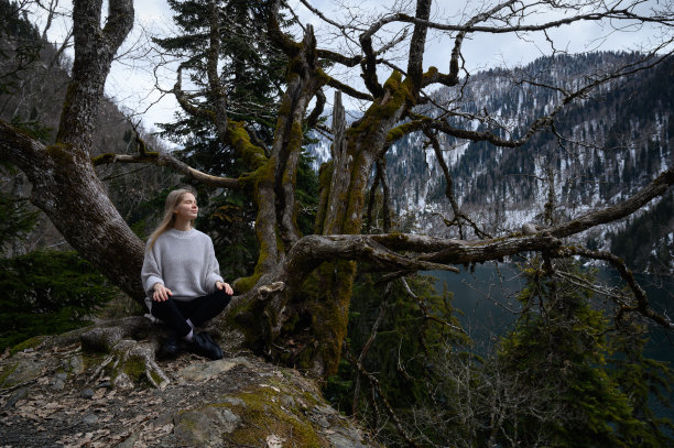 女孩坐在一棵树上，在蓝色的湖背景上沉思。阿布哈兹的Ritsa湖图片下载