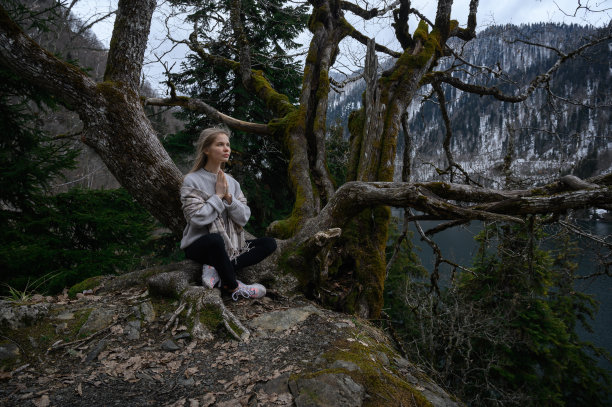 女孩坐在一棵树上，在蓝色的湖背景上沉思。阿布哈兹的Ritsa湖图片下载