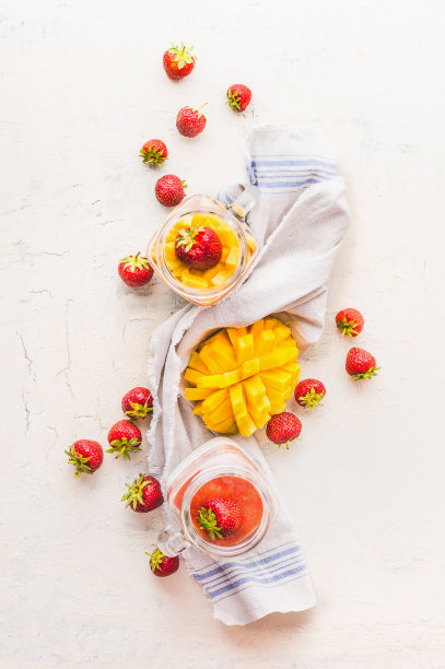 白色的桌子上放着装满酸奶布丁、芒果和草莓的玻璃罐子。图片下载