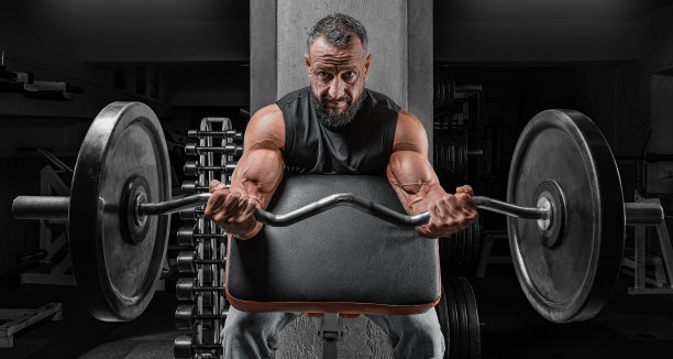 健壮的男人坐在健身房的长凳上，举着杠铃，锻炼二头肌，健身和健美概念图片下载