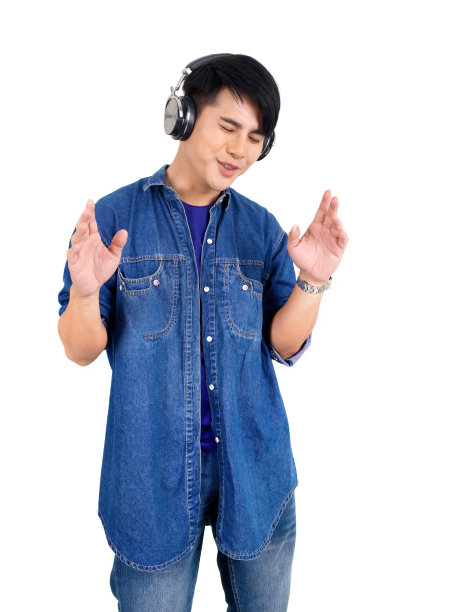 年轻的亚洲男子一边听着耳机里的音乐，一边跳舞，摇摆，有节奏地举起手臂。肖像在白色背景与工作室灯光。图片下载