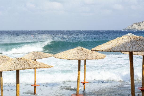 在暴风雨的海面附近的海岸上有几把稻草遮阳伞。夏日的岸边撑着几把雨伞图片下载