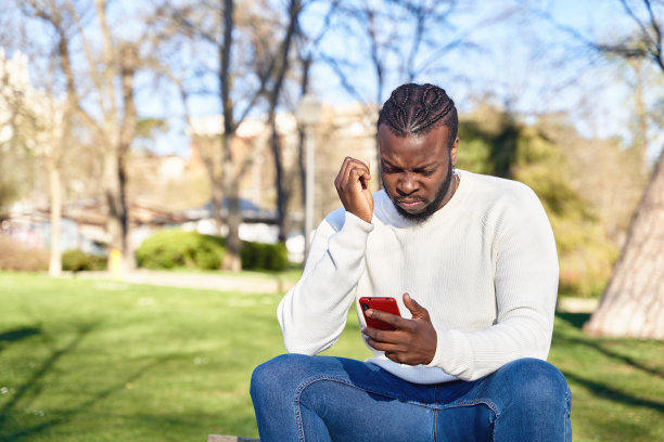 非裔美国人坐在公园的长椅上看他的手机。关注的年轻人。技术的概念图片下载