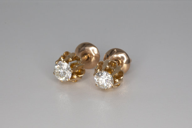 特写的黄金耳钉与白色水晶和钻石。漂亮的金色耳环上的灰色背景图片下载