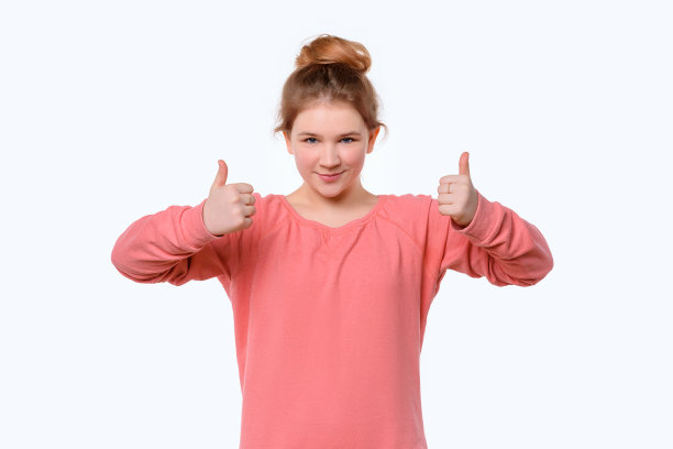 一个可爱的年轻女孩的肖像在粉红色休闲运动衫显示拇指向上。白色背景图片下载