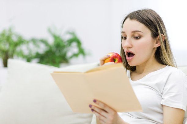 一名孕妇咬着苹果，手里拿着一本书。图片下载