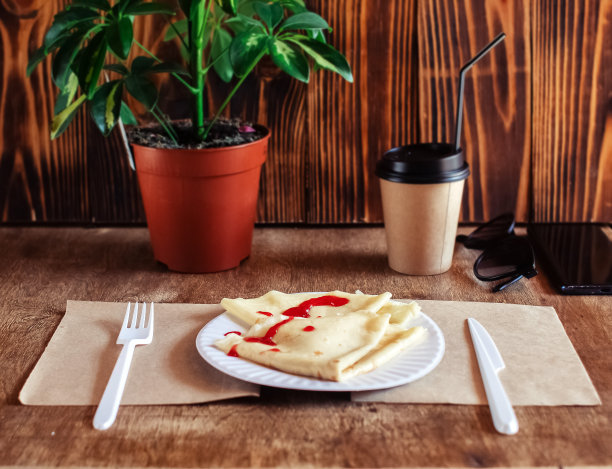 餐馆里的盘子上淋着红糖浆的煎饼。在咖啡馆吃早餐。一个女人用一次性餐具吃煎饼当早餐。俯视图和垂直照片图片下载