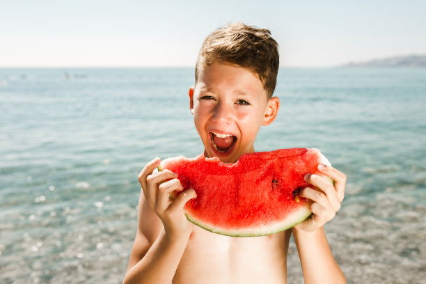快乐的孩子在海上吃着多汁的西瓜。图片下载