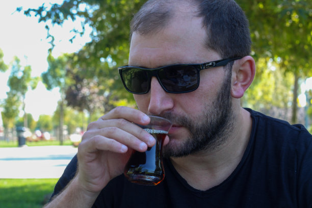 戴着太阳镜喝着气泡茶的大胡子男人戴着绿色的细腰玻璃杯图片下载