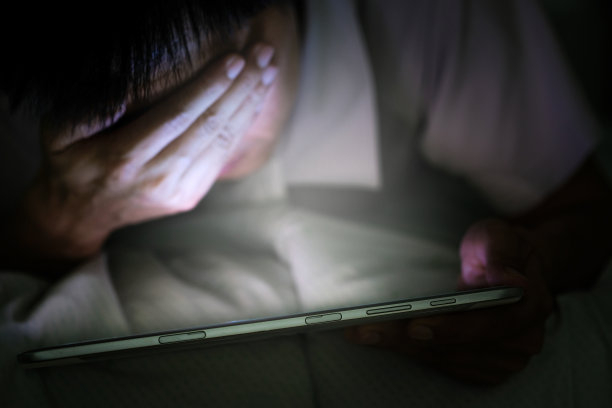 女人不睡觉，晚上压力很大。她在没有光线和黑暗的卧室里使用和查看智能手机。图片下载