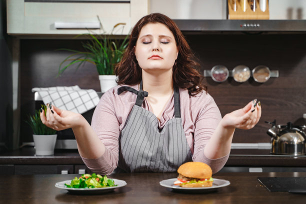 一幅大号女人闭着眼睛在厨房里选择汉堡还是沙拉的照片。意志力、减肥和饮食观念图片下载