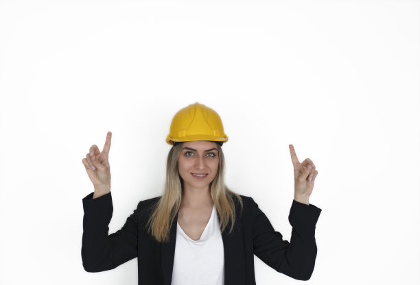建筑女指着手和手指向上看相机，她的脸上带着大大的笑容戴着安全帽孤立在白色的背景。图片下载