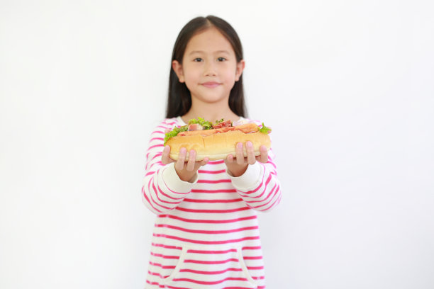 白色背景上的亚洲小女孩为你抱着热狗的肖像。专注于儿童手上的食物图片下载
