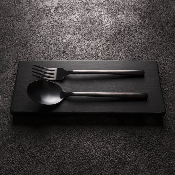 黑色哑光叉子勺子特写。深色背景，现代餐具，方形照片图片下载