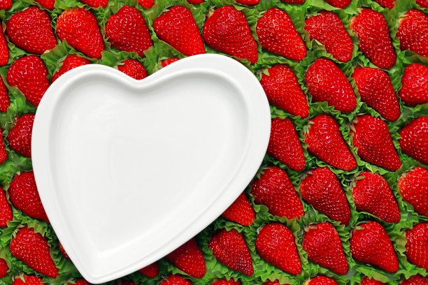 一排排摆放着美味的成熟红草莓。以草莓为背景的心形白色空盘子。图片下载
