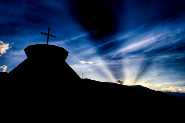 塔和十字架的深色轮廓，背景是阳光和蓝黑色天空图片下载