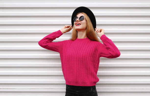 肖像快乐微笑的年轻女子模特穿着粉红色针织毛衣和黑色圆帽在白色的背景图片下载