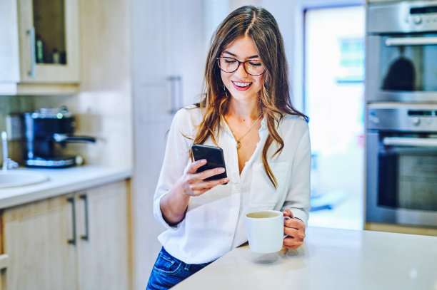 这是一个年轻女子在家里一边喝咖啡一边使用智能手机的照片图片下载
