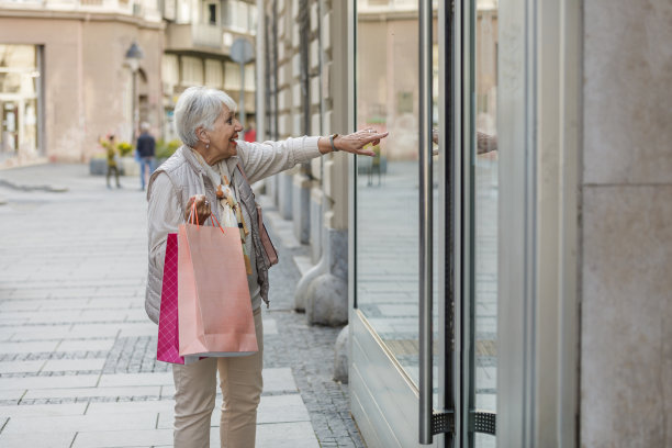 一个快乐的老妇人的肖像是站在购物窗口和浏览商店。图片下载