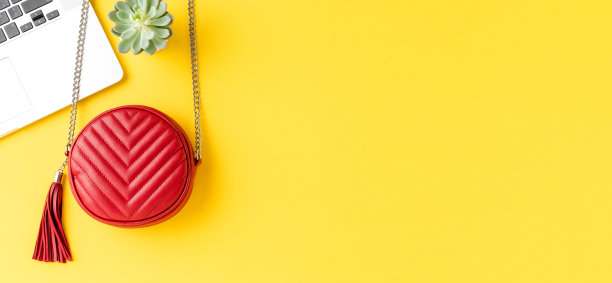 时尚背景与红色女人的钱包与笔记本电脑和小绿色多汁在黄色的桌面。横幅图片下载