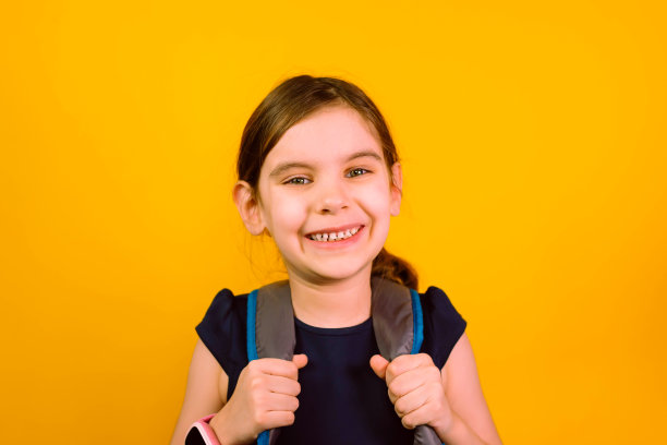 带着智能手表的小女孩在黄色背景下独自看着摄像头。回到学校。图片下载