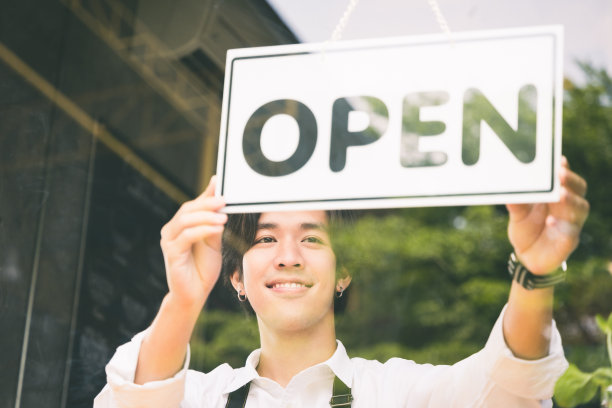 年轻的亚洲男子翻转打开的标签，欢迎顾客，并在早上打开咖啡馆。男亚洲咖啡师用镜子打开门口的咖啡馆。图片下载