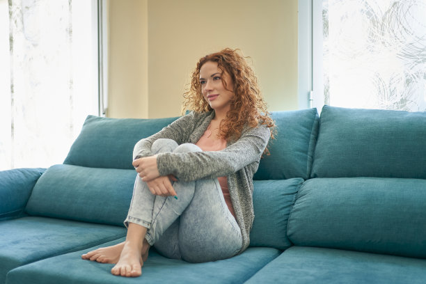 漂亮女人盘腿坐在沙发上看电视。在家放松的概念图片下载