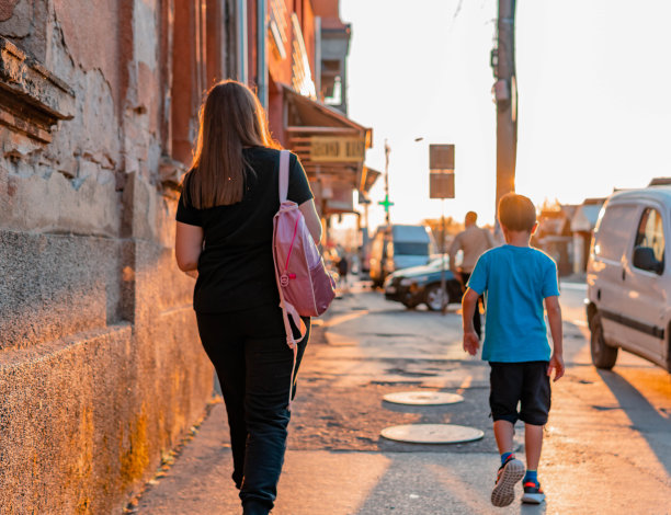 母亲和儿子步行上下学。母亲背着儿子的背包。阳光明媚的城市图片下载