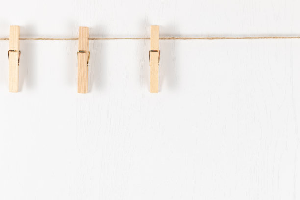 三根带有金属弹簧的木制晾衣夹挂在白色背景上的一根绳子上图片下载