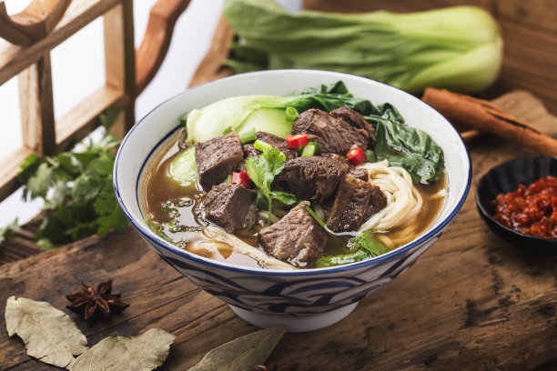 木桌上的碗里放着麻辣的红汤牛肉面图片下载