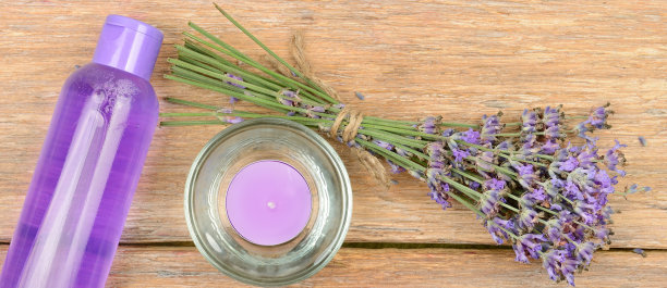 木桌上放着一束薰衣草花、香薰蜡烛和薰衣草香波。宽的照片。图片下载