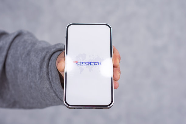 手机显示与突发新闻图标在灯光背景。一名男子手里拿着一个智能手机模型。图片下载