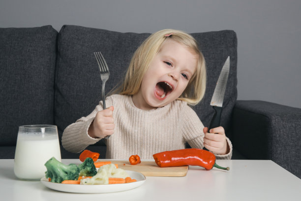 可爱的快乐的蹒跚学步的小女孩拿着刀叉吃健康的蔬菜餐图片下载