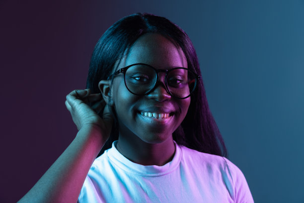 年轻的非洲美丽女孩的肖像孤立在黑暗的背景在混合霓虹灯。图片下载