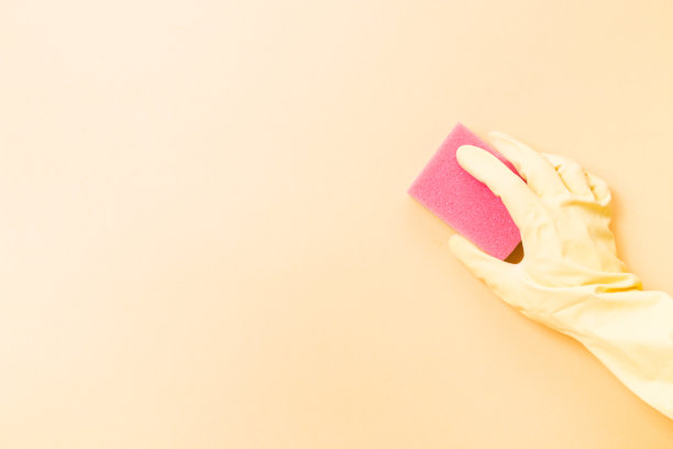 手握黄色橡胶手套的橙色海绵用于洗碗和清洁，黄色背景拷贝空间，清洁概念，家居护理，春季大扫除图片下载